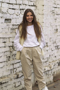 Portrait of smiling young woman standing against brick wall