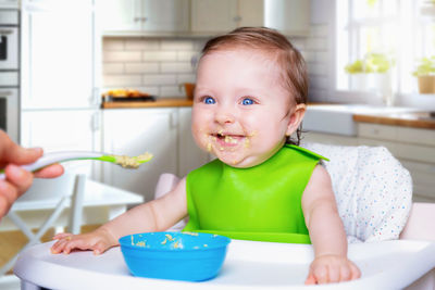 Cropped hand feeding baby girl in kitchen at home