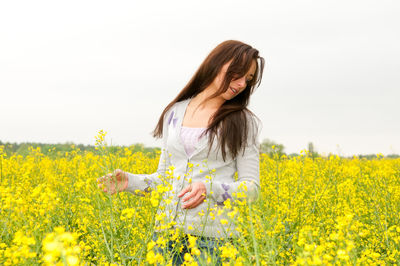 Woman standing at rape field against clear sky