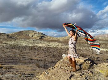 Young woman holding shawl while standing on rock formations at mojave desert