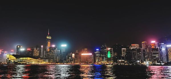 Illuminated buildings by river against sky at night