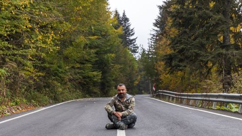 Full length of man sitting on road amidst forest