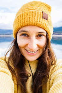 Closeup of carefree smiling woman wearing sweater and yellow wool hat taking a selfie