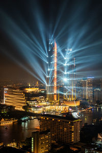 Illuminated city by river against sky at night