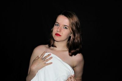 Portrait of shirtless woman covering breasts with towel against black background