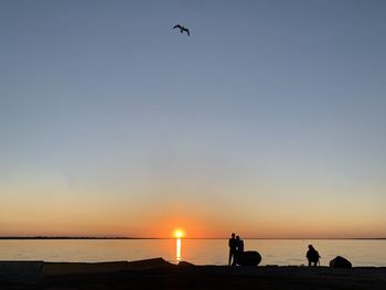 Silhouette people on beach against sky during sunset