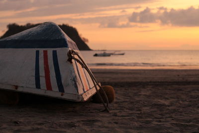 Abandoned upside down boat at beach against sky during sunset