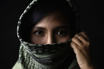 Close-up portrait of young woman wearing scarf against black background