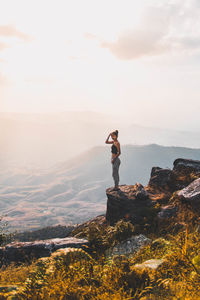 Woman standing on rock at mountain against sky