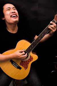 Musician playing guitar against black background