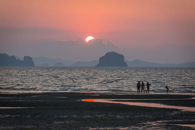 People on beach against sky during sunset