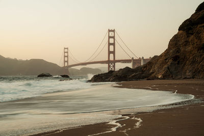 Suspension bridge over sea against sky during sunset