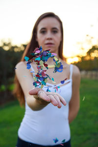 Portrait of young woman throwing confetti at park