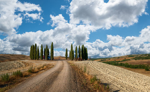 Dirt road amidst field against sky