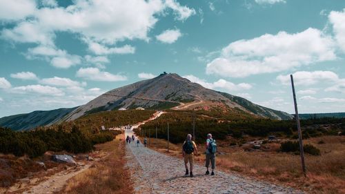 Rear view of people walking on mountain against sky