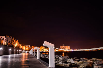 Illuminated buildings by street against sky at night