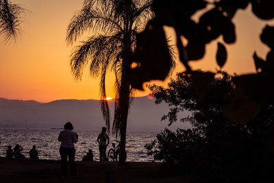 Silhouette people looking at sea against sky during sunset