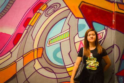 Young woman standing against graffiti wall