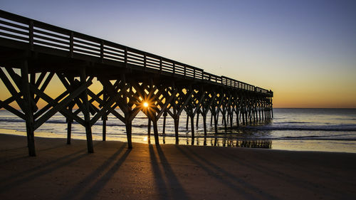 Silhouette pier on beach against clear sky during sunset