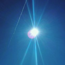 Low angle view of sun shining through blue sky