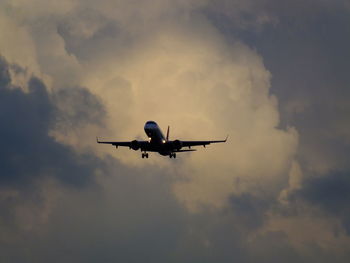 Low angle view of airplane flying against cloudy sky