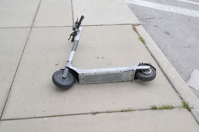 Scraped up silver electric scooter lying down on sidewalk