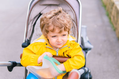 Cute boy sitting with food in baby carriage outdoors