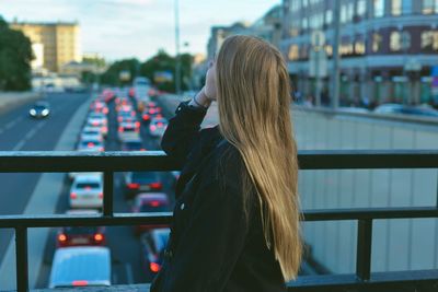 Rear view of woman standing by railing in city