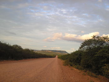 Empty road along trees and landscape against sky