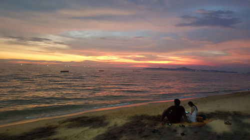 People at beach against sky during sunset