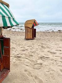 Hooded chairs on beach against sky