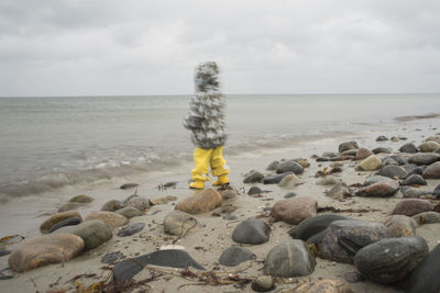 Rear view of man on rocks at beach against sky