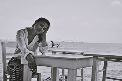 Young woman on table at beach against sky