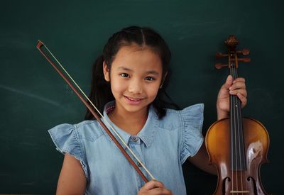 Portrait of smiling girl holding violin against wall