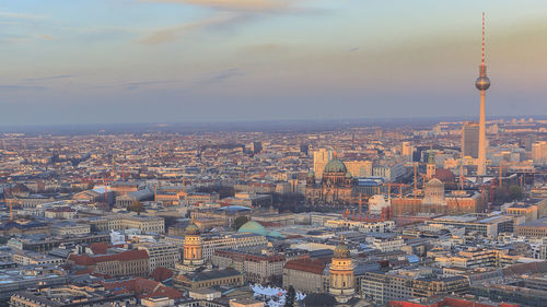 Fernsehturm amidst cityscape against sky during sunset