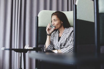 Mature businesswoman drinking water while sitting on chair at creative office