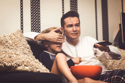 Father closing son eyes while watching tv at home