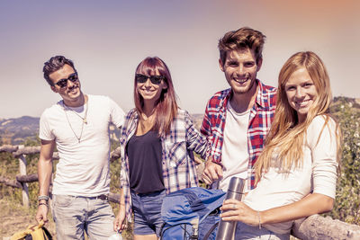 Portrait of smiling friends standing against sky