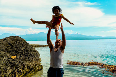 Father playing with daughter while standing at beach against sky