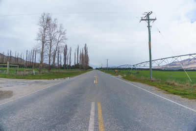 Road by electricity pylon against sky