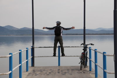 Full length of man standing on railing by sea against sky