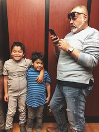 Father using mobile phone while sons standing indoors