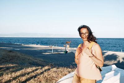 Young woman with backpack smiles on the beach and looks into the camera. summertime and traveling. 