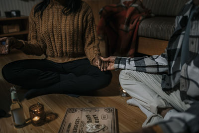 Midsection of multiracial friends holding hands sitting in haunted house