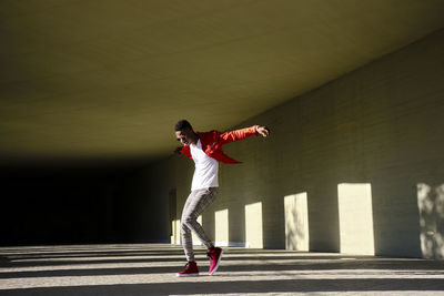 Young man in red jacket in front of concrete building in sunlight