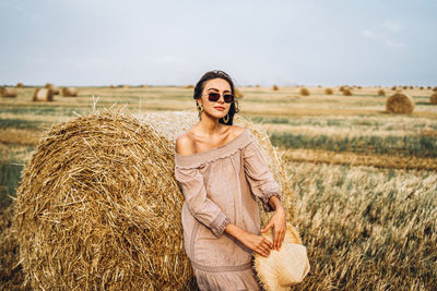 Smiling woman in sunglasses with bare shoulders on a background of wheat field and bales of hay.