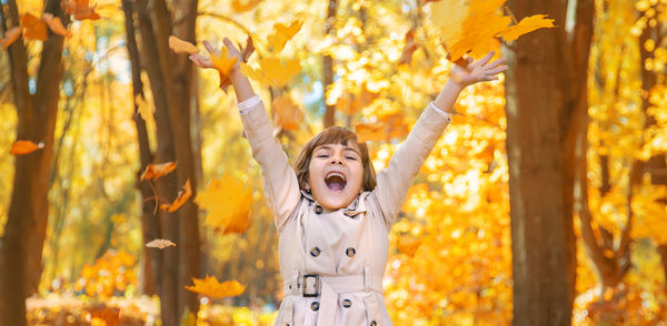 Cute girl holding leaves against trees