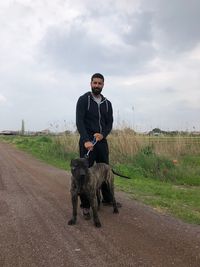 Full length portrait of man with dog on dirt road against sky