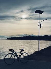 Bicycle by lake against sky during sunset