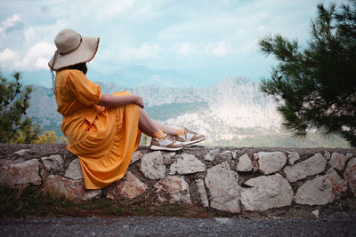 Rear view of woman sitting on rock against sky